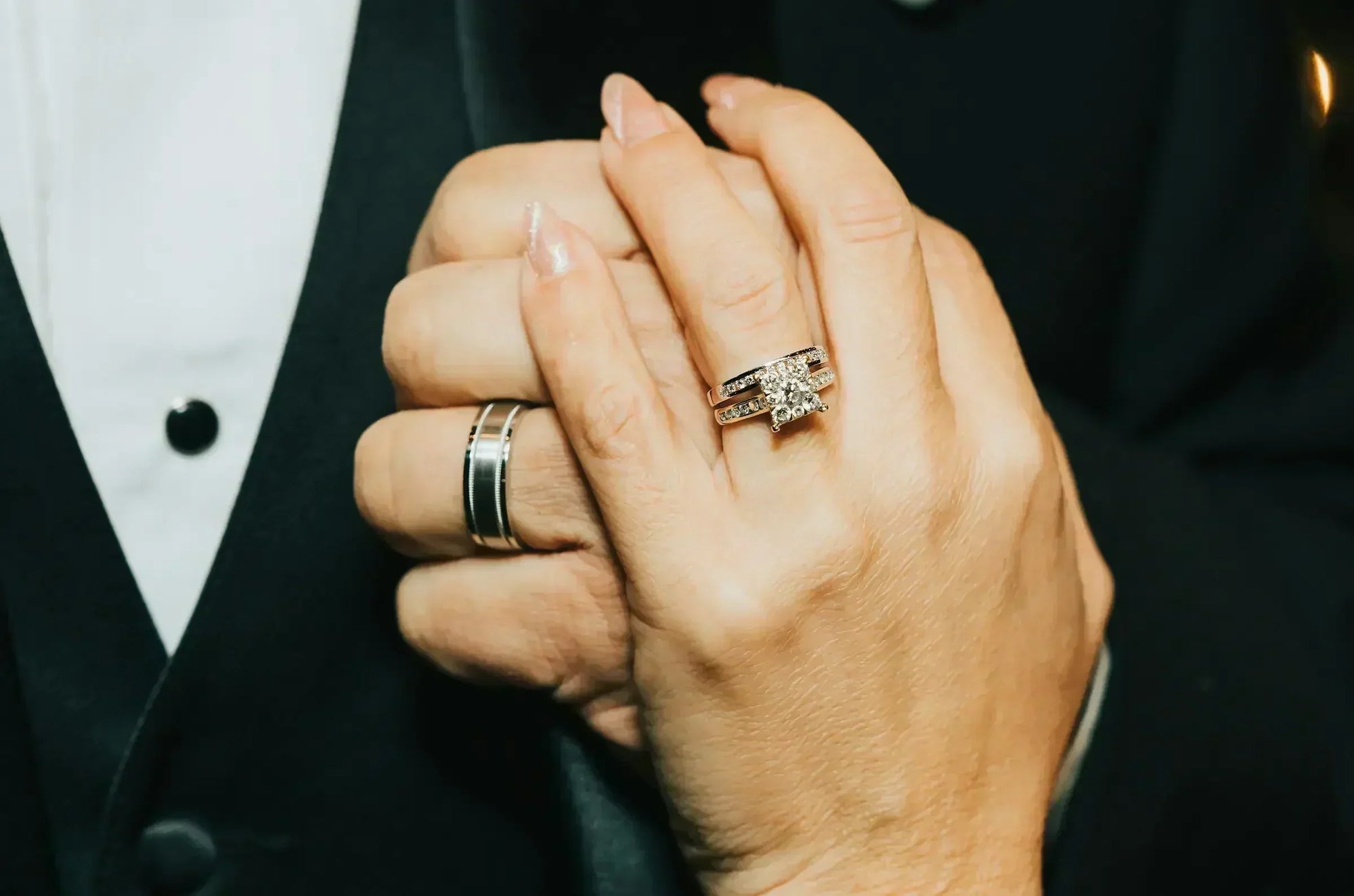 couple holding hands showing diamond engagement ring and wedding bands