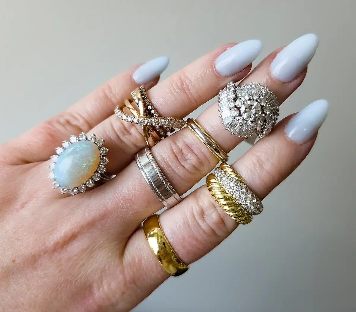 Person wearing multiple rings, including a large white opal ring, a silver band, a twisted gold ring, and a textured silver ring with clear stones.
