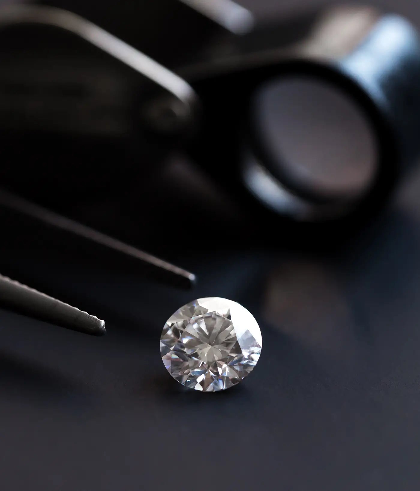 Round Diamond on a dark surface with tweezers and a magnifying glass in the background
