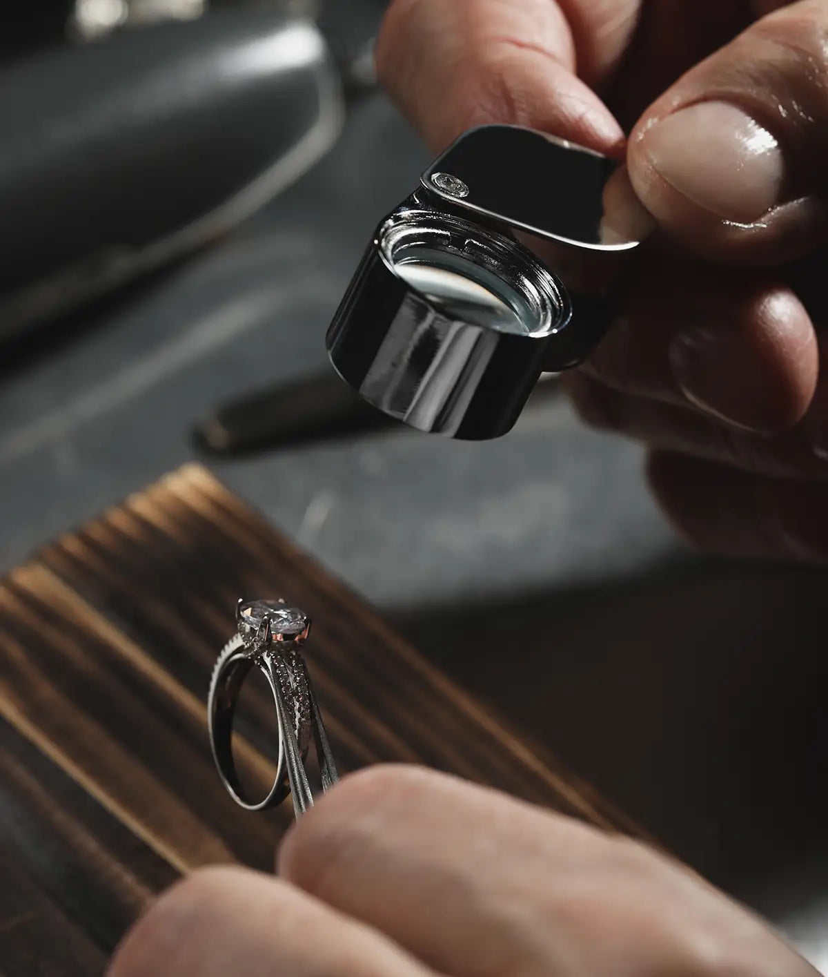 A close-up of a jeweler using a black and silver loupe to examine an engagement ring.