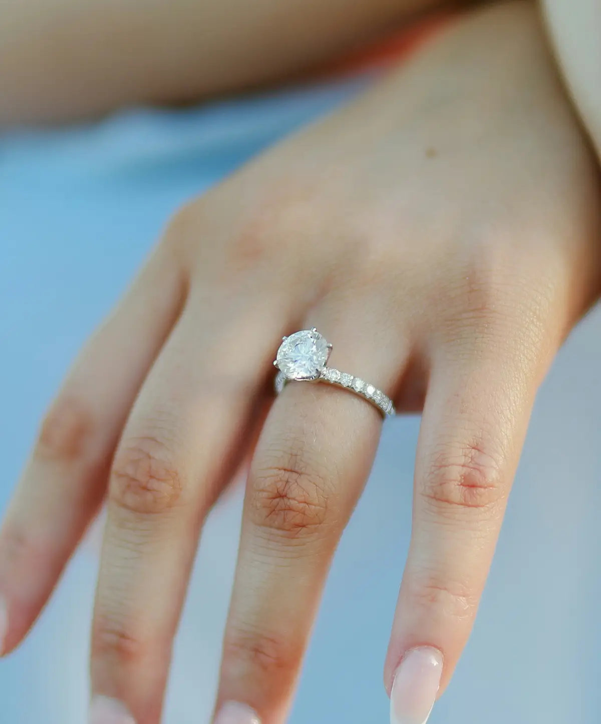 Close-up of a hand wearing a round diamond ring with diamonds on the side of the band.