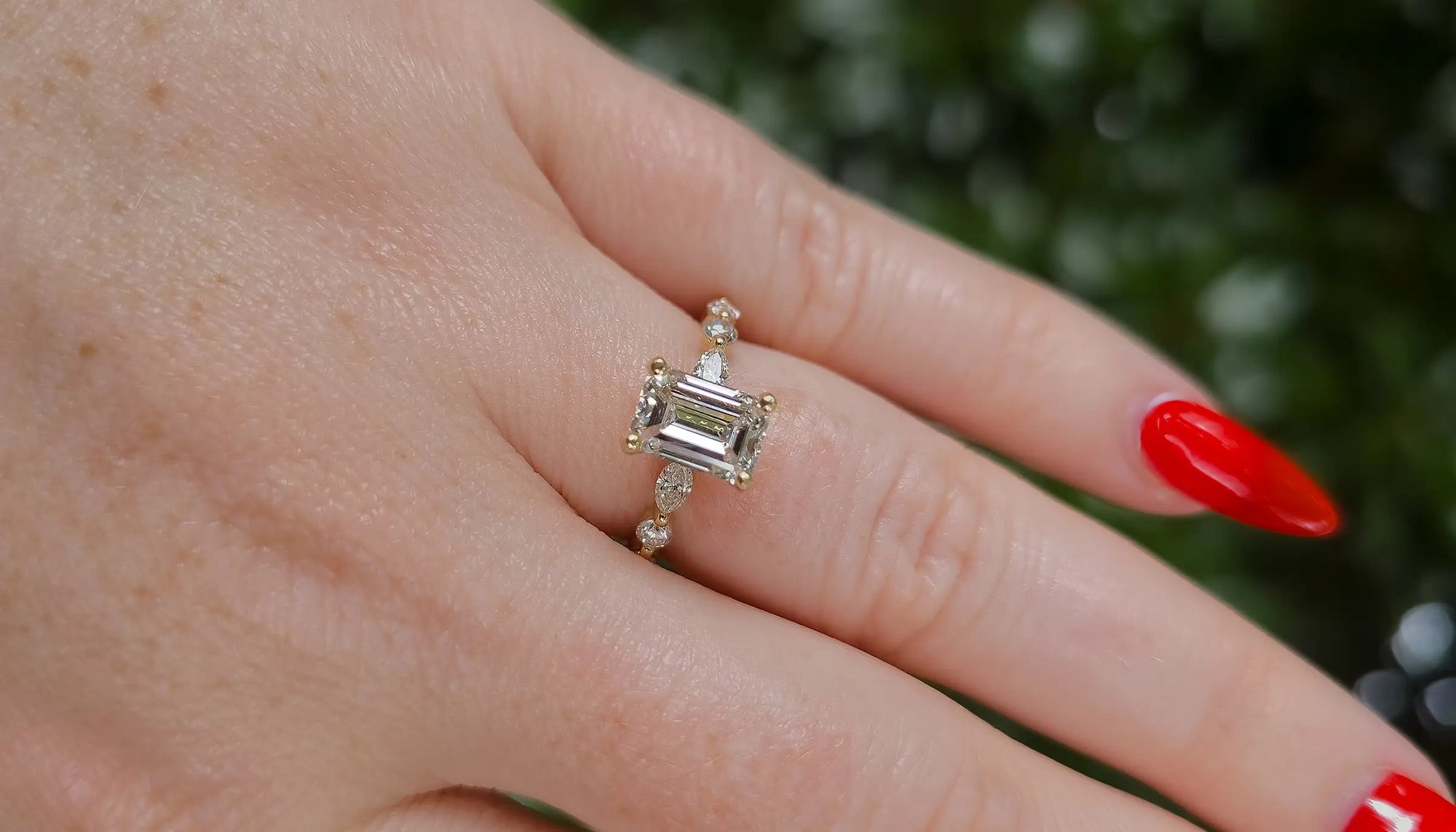 Close-up of a hand wearing a emerald diamond ring with an accented band