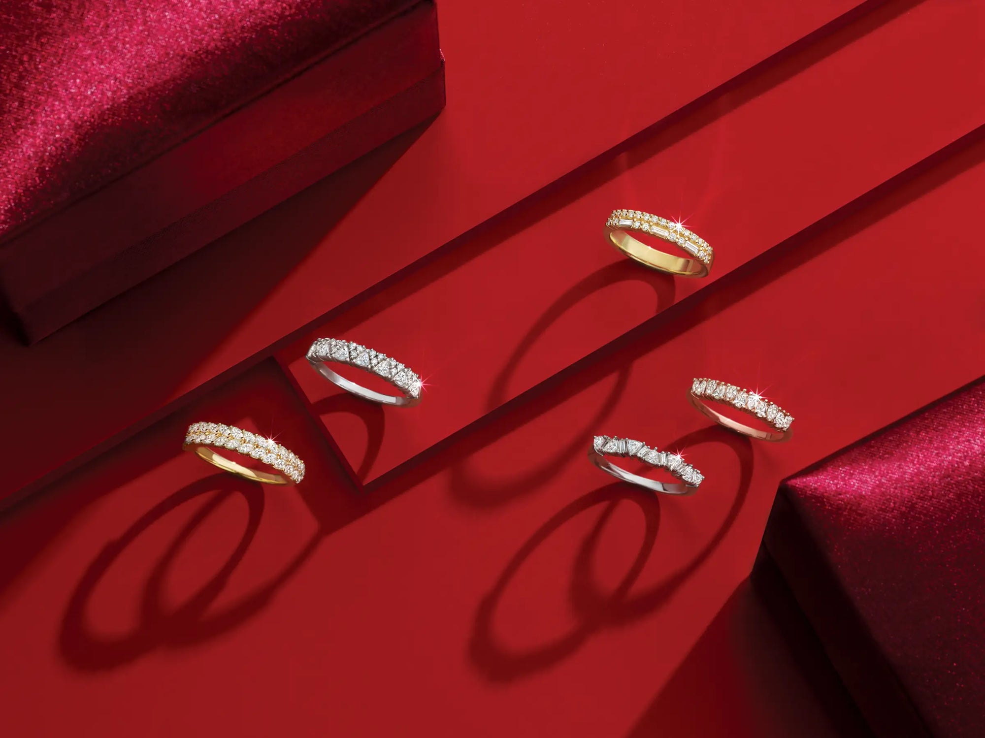 Gold and silver diamond rings on a red surface with a jewelry box.